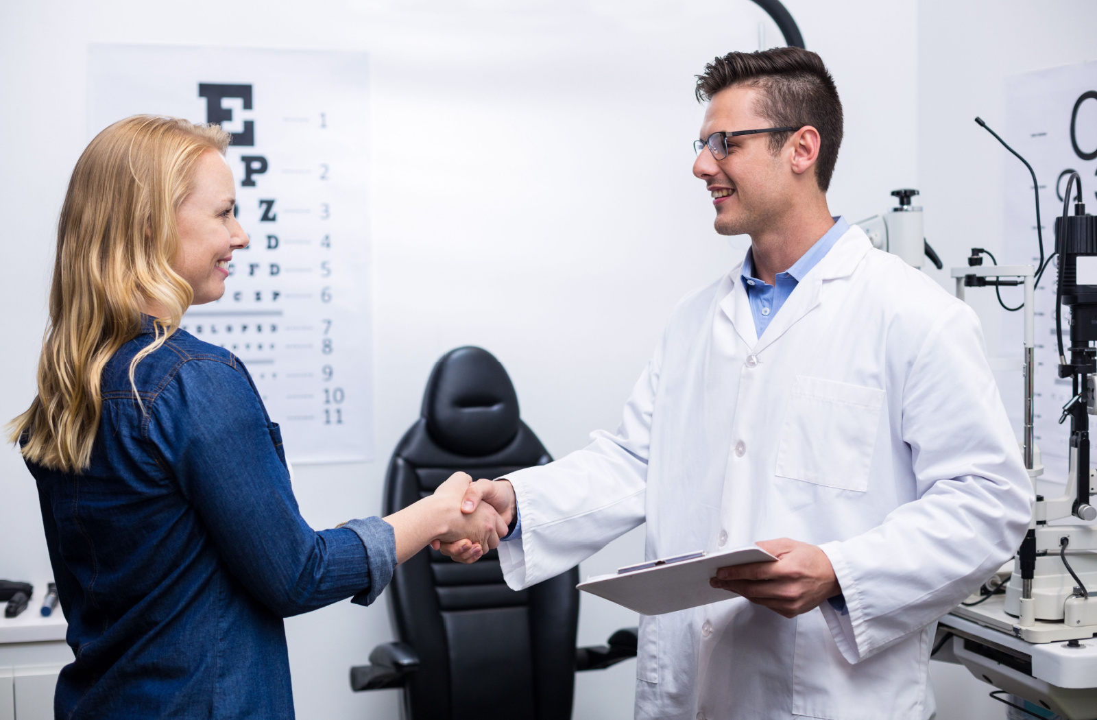 A woman in an optometry clinic shaking hands with her male optometrist.