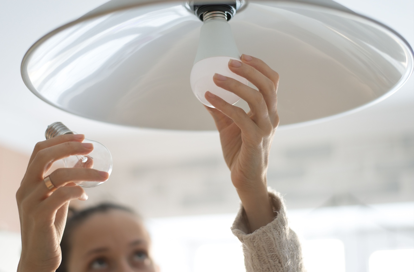 A woman putting a LED bulb using her left hand while her right hand is holding a standard fluorescent bulb