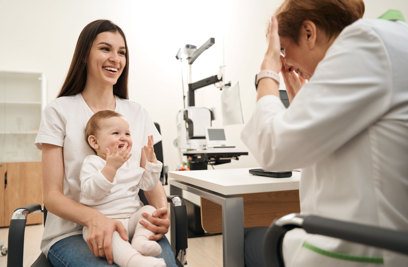 An infant sitting comfortably in their parents' lap, smiling during their first routine eye exam.