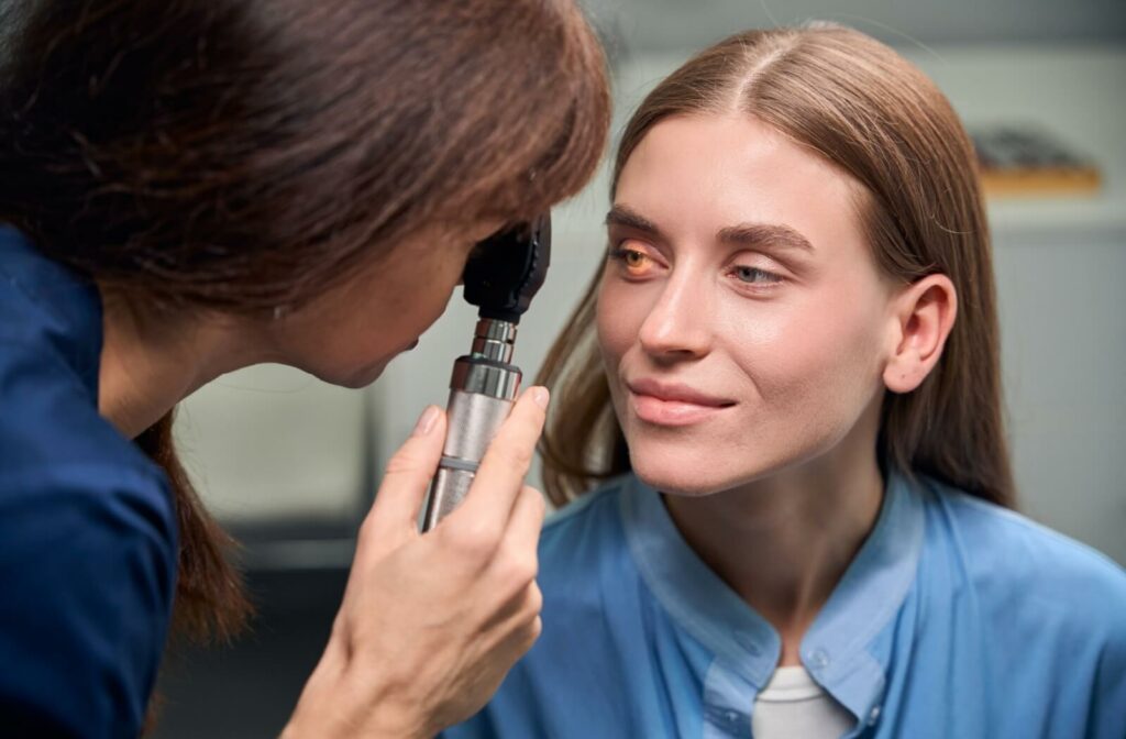 An eye care professional using a handheld ophthalmoscope to examine a patient's eye in a clinical setting.
